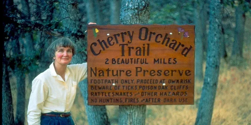 Nancy with the hand-carved trail sign at what is today Friends of the Columbia Land Trust's Lyle Cherry Orchard preserve.